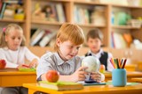 Little redhead schoolboy behind school desk during lesson