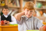 Little redhead schoolboy behind school desk 
