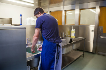 Kitchen porter washing up at sink
