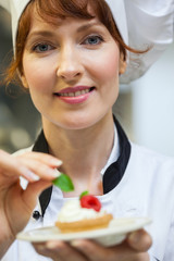 Gorgeous head chef putting mint leaf on little cake on plate