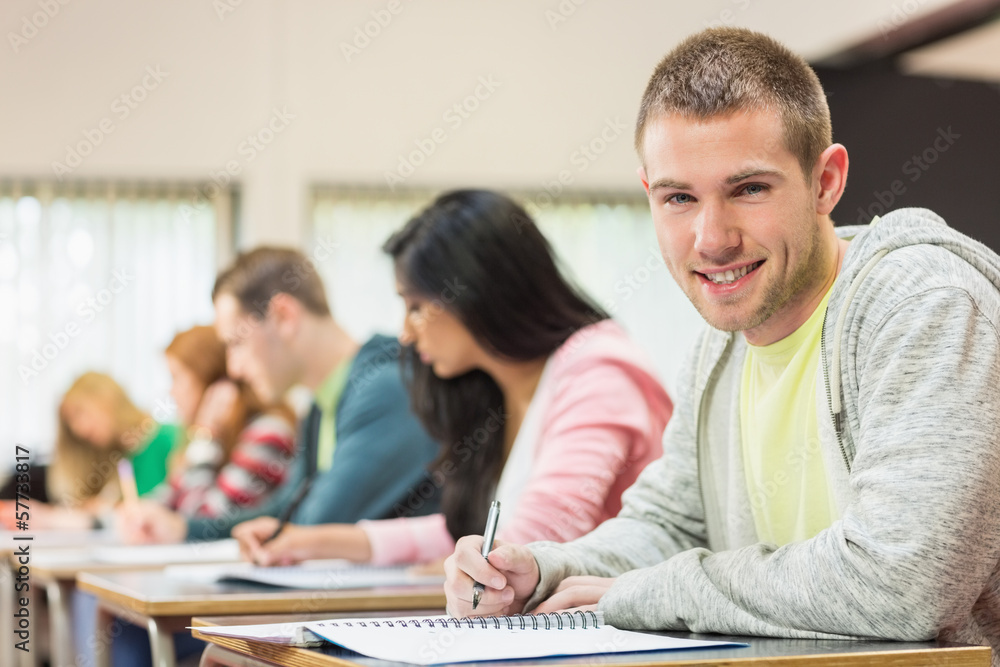 Poster smiling male student with others writing notes in classroom