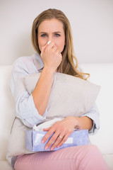Fototapeta premium Frowning casual blonde sitting on couch blowing nose