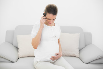 Young pregnant woman phoning while holding her belly and looking