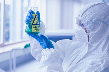 Scientist in protective suit with hazardous chemical in flask at