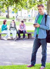 College boy text messaging with blurred students in park