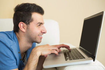 Casual smiling man sitting on couch using and looking at laptop