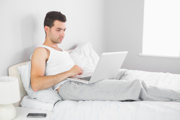 Handsome calm man using laptop in his bed