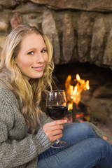 Beautiful woman with wineglass in front of lit fireplace