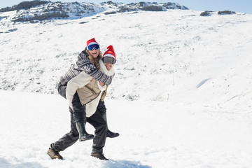 Fototapeta na wymiar Full length of a man piggybacking cheerful woman on snow