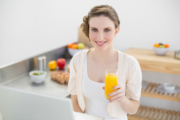 Joyful brunette woman holding a glass of orange juice while sitt