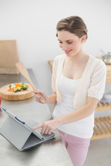 Smiling brunette woman using her tablet while standing in her ki