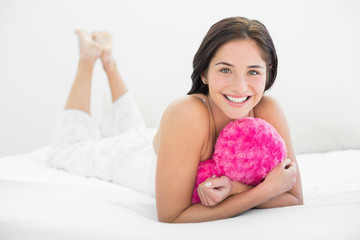 Obraz na płótnie Canvas Smiling woman lying in bed with heart shaped pillow