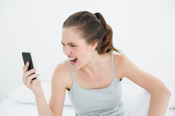 Fototapeta premium Woman shouting into mobile phone in bed