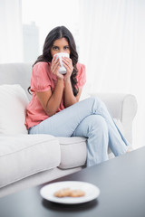 Calm cute brunette sitting on couch drinking from mug