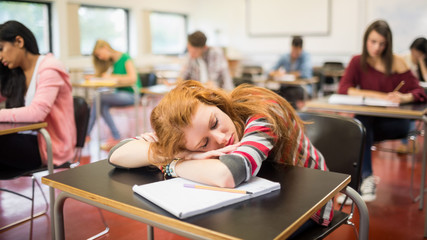 Blurred students in the classroom with one asleep girl