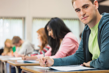 Male student with others writing notes in classroom