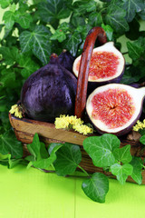 Ripe figs in basket leaves on wooden table close-up