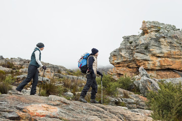 Couple walking through rocky landscape with trekking poles again
