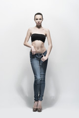 A beautiful woman in jeans posing in studio over grey background