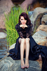 Gorgeous girl in black lace dress sitting on a rock