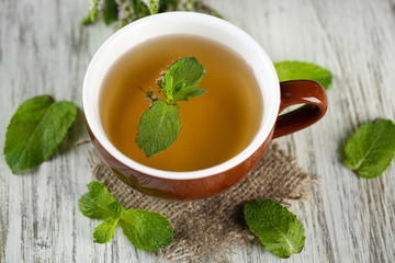 Cup of herbal tea with fresh mint flowers on wooden table