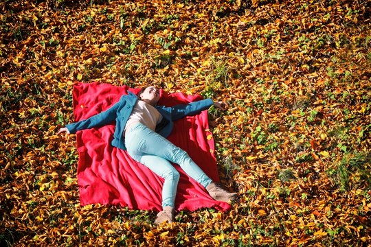 Young girl relaxing in autumnal park lying on red blanket