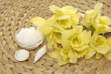 Fototapeta na wymiar Bowl of bath salt with seashell and yellow orchid on mat background
