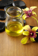 Massage stones and essential oil with orchid flowers on wooden board