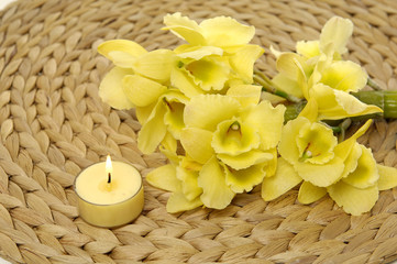 burning candle and branch yellow orchid on woven mat 

