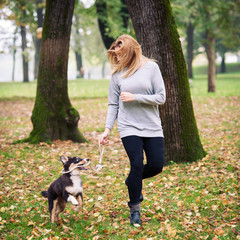 Naklejka na ściany i meble Young woman playing with Australian Shepherd dog outdoors in the