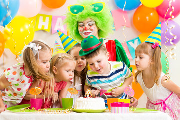 children with clown celebrating birthday party and blowing candl