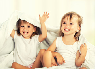 happy little girls twins sister in bed under the blanket having © JenkoAtaman