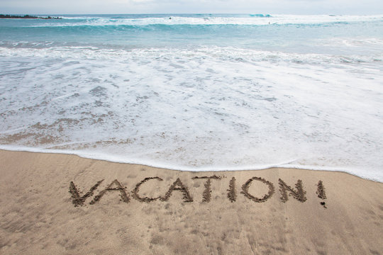 Vacation! A message written in the sand on beach.