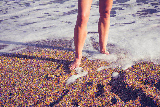 The legs of a young woman walking in the surf on beach