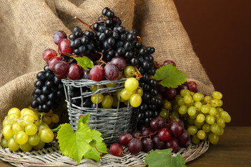 assortment of ripe sweet grapes in basket, on brown background