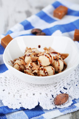 Many toffee in bowl on napkin on wooden table