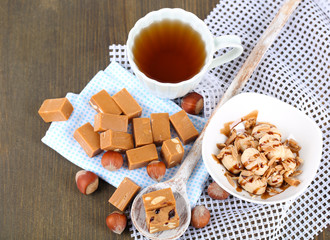 Many toffee in spoon and cup of tea on napkins on wooden table