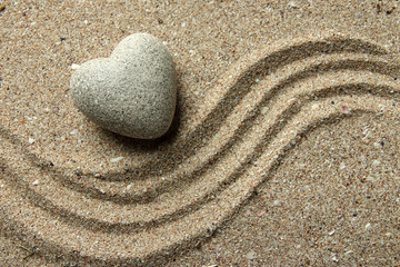 Fototapeta na wymiar Szary Zen stone w kształcie serca, na tle piasku