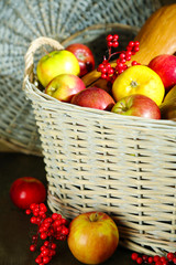 Juicy apples and pumpkin in wooden basket on table close-up