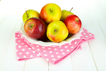 Juicy apples on plate on white wooden table