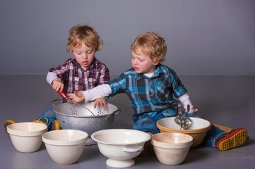 Cute blonde twins squabbling over cooking bowls and utensils