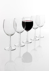 Glass filled with red wine in a row of empty glasses