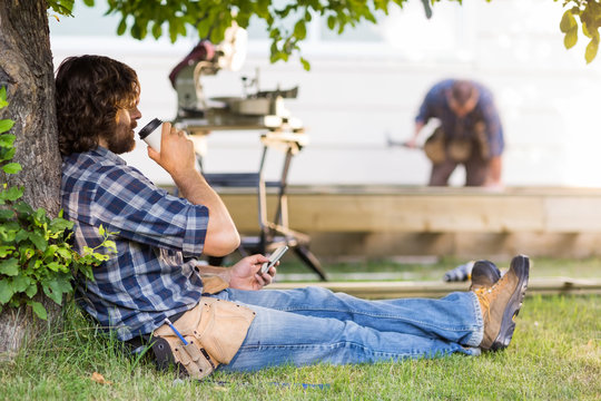 Carpenter Using Mobilephone While Drinking Coffee From Disposabl