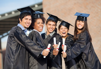 Fototapeta Students In Graduation Gowns Showing Diplomas On Campus obraz