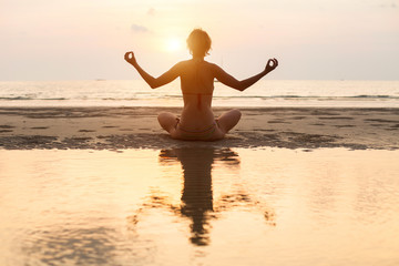 Yoga woman sitting in lotus pose on the beach during sunset