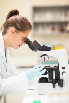 Focused brunette student looking through microscope