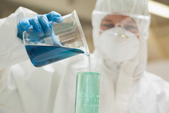 Lab assistant with mask mixing blue liquid in beaker
