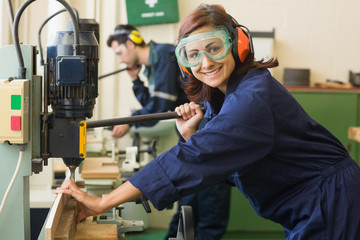 Smiling trainee with safety glasses drilling wood