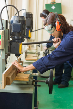 Female carpenter drilling wood in workshop