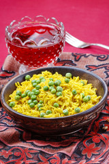 Indian cuisine: bowl of yellow rice with green peas on red backg